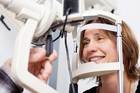 A woman is smiling while having her eyes examined by an ophthalmologist.