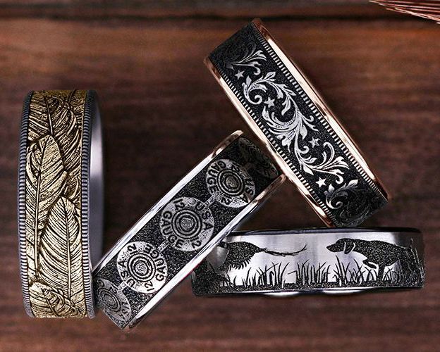Four intricately designed metal rings: feather, floral, bullet casing, and hunting dog engravings.