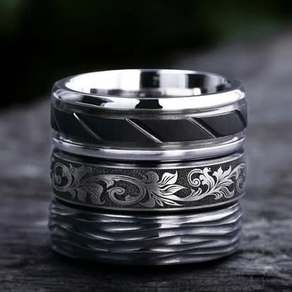 Three stacked silver rings with different engraved textures on a wood surface.