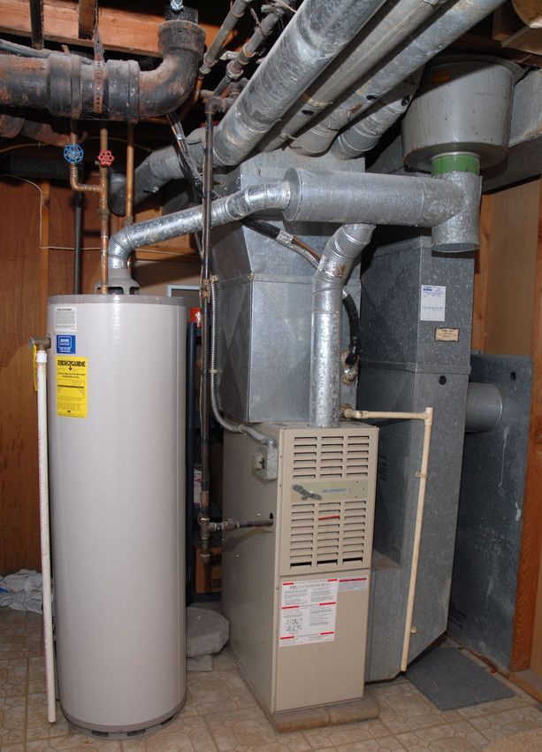 Water heater and furnace in basement with various pipes and ductwork overhead.