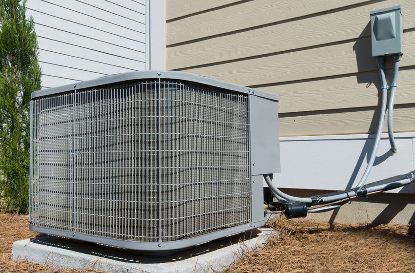Air conditioning unit near a house, gray and beige, set on a concrete pad.