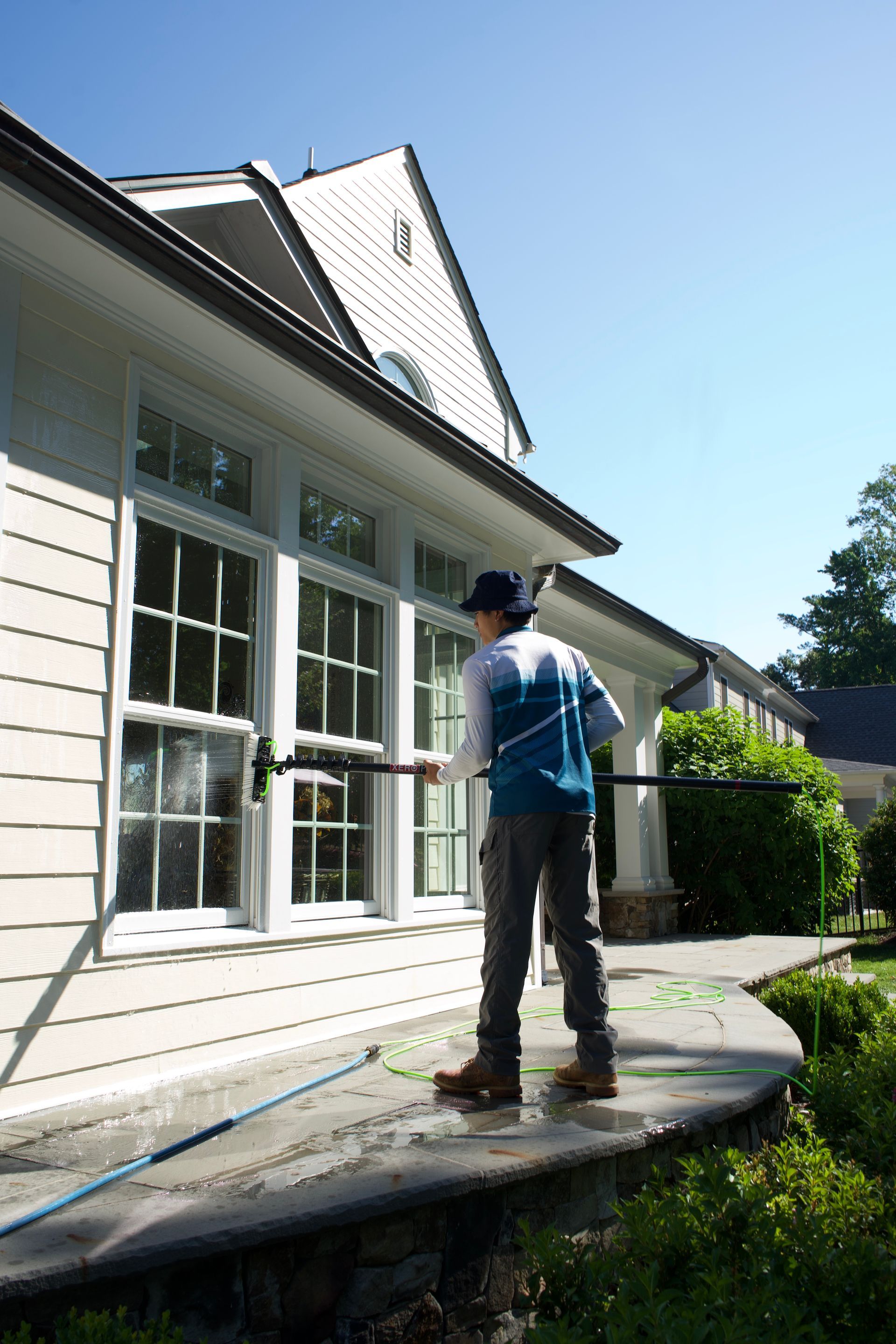 Person painting the exterior of a house on a curved roof edge in bright sunlight