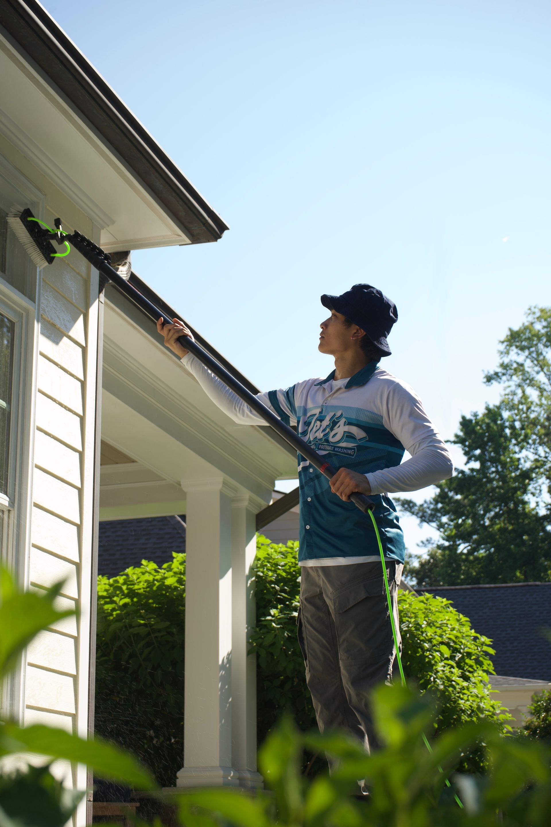 Person using a hose to clean house siding in a sunny yard