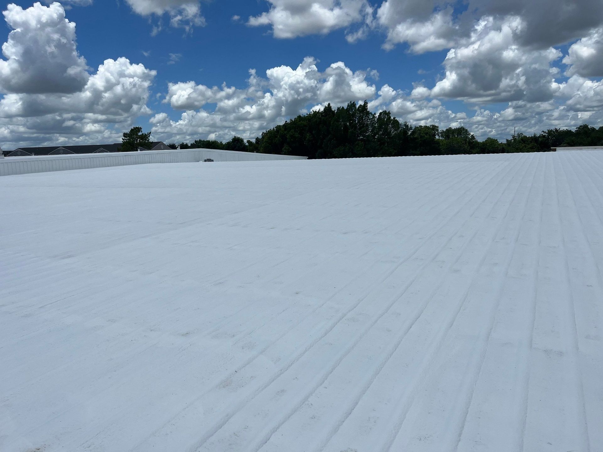 A large white roof with trees in the background and a blue sky with clouds.