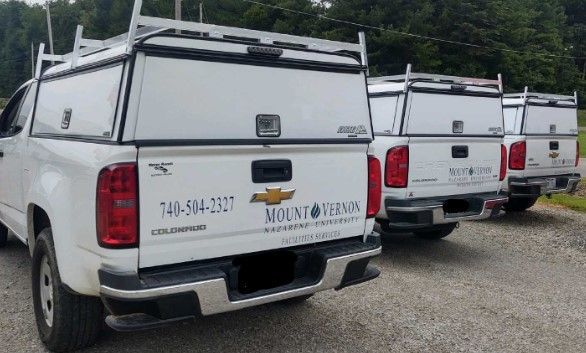 A row of white trucks was parked next to each other on a gravel road.