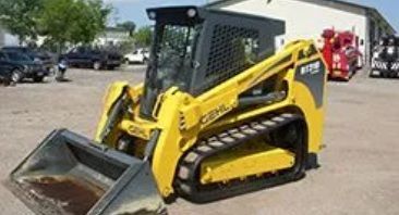 Yellow and black track skid steer with a bucket on a paved surface.