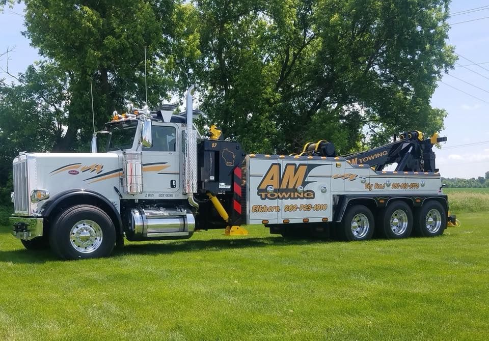 White AM Towing truck parked on grass.  Green trees in the background.