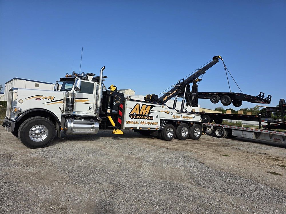 White tow truck lifting a trailer on a gravel lot under a blue sky. 
