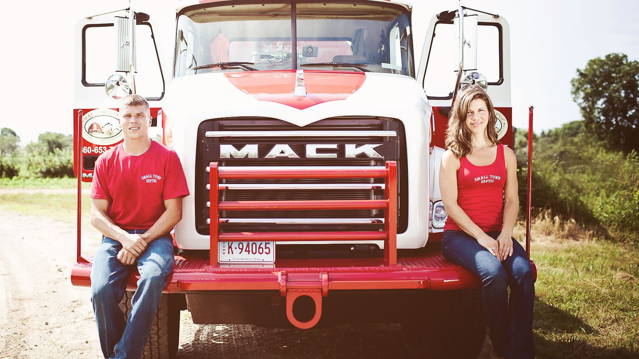 Two people in red shirts sit on a red truck, the front displaying the name