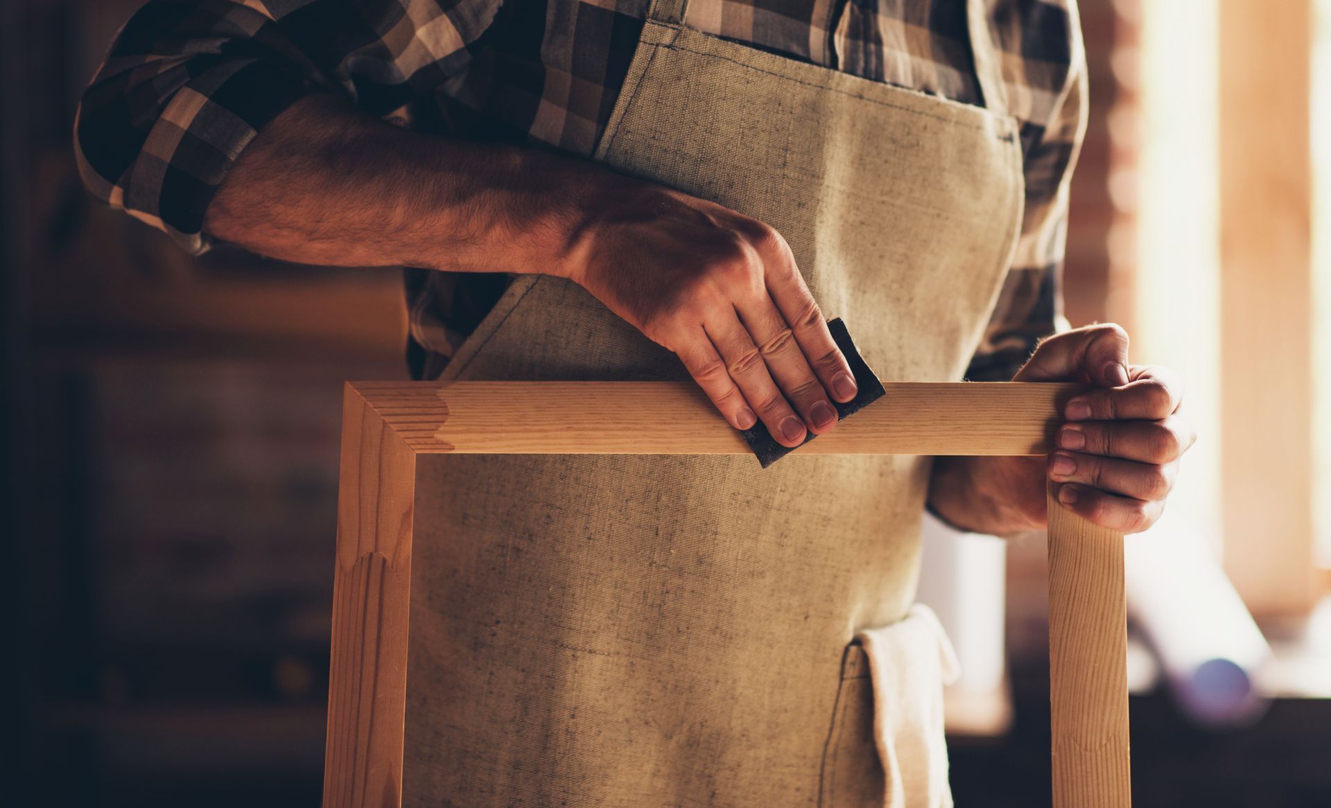 A man is sanding a wooden frame with a sandpaper.