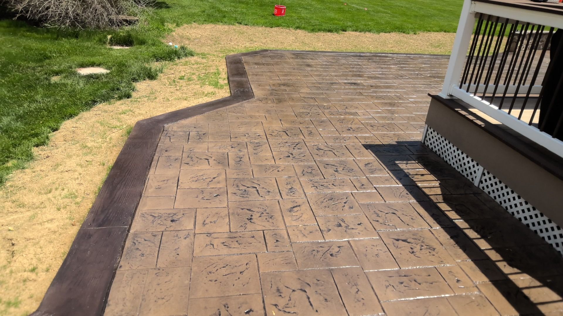 Stamped concrete patio beside a grassy yard, with a small porch and steps on the right.