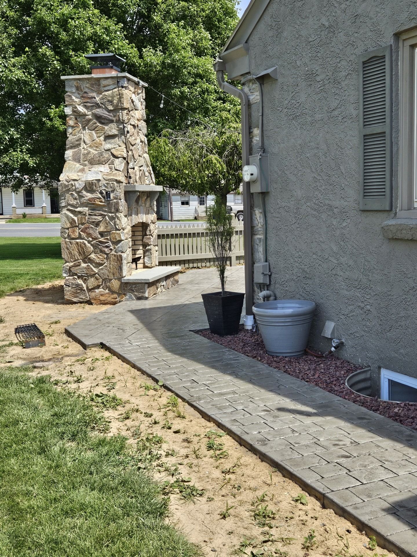 Stone walkway beside a gray house, with a brick pillar and potted containers in the yard.