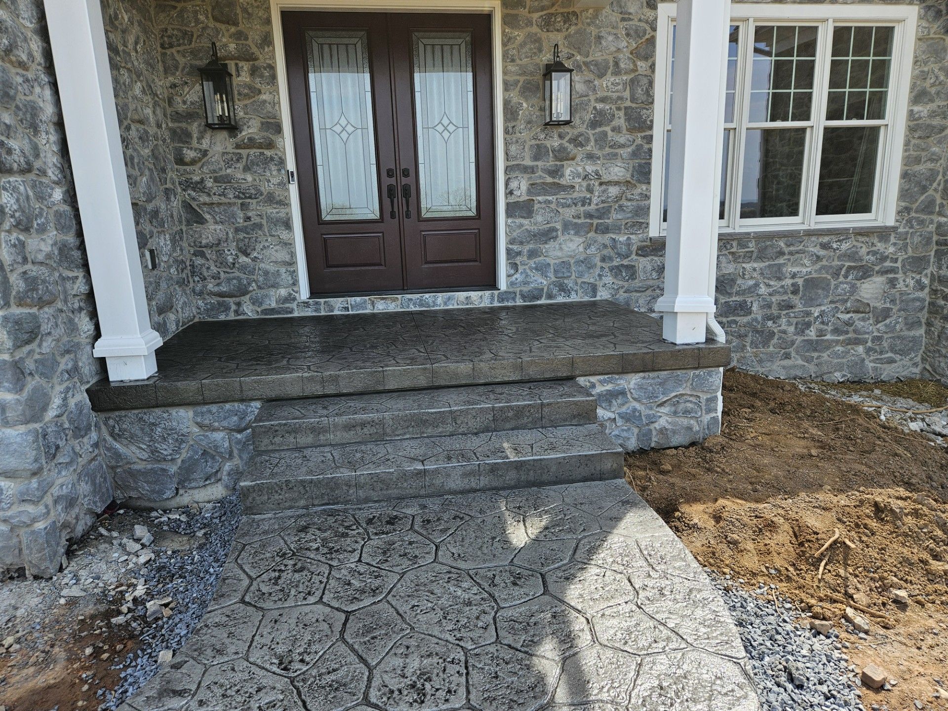 Stone front porch with double doors, steps, and a cracked concrete walkway leading to the entrance.