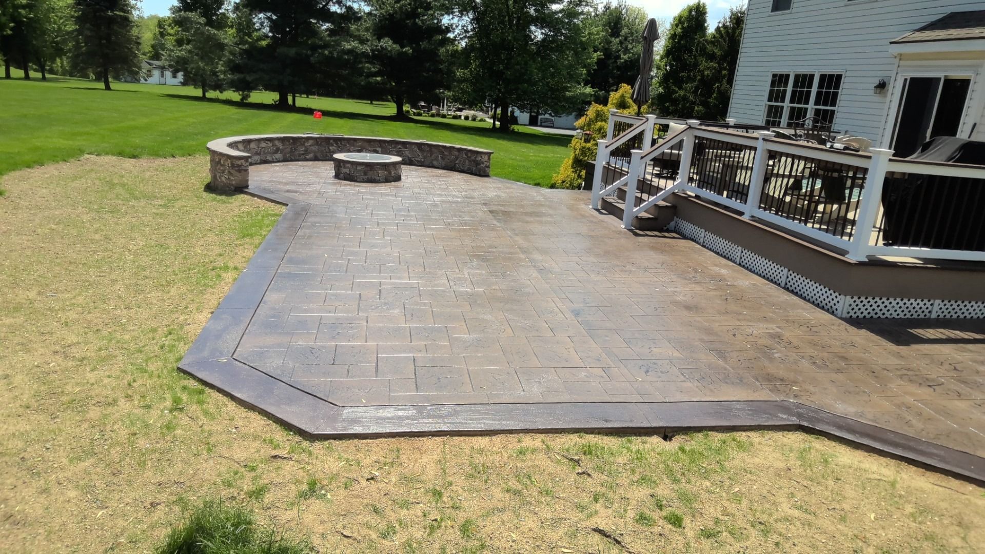 Stamped concrete patio beside a house, with a curved stone seating wall and grassy yard.