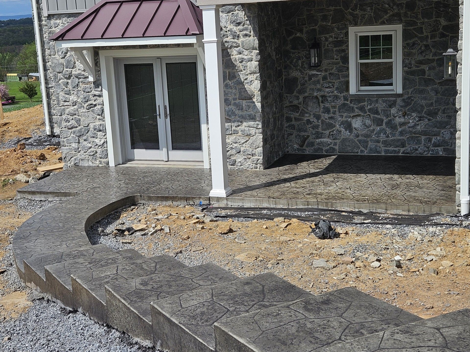 Stone-front house under construction with a curved gravel path and porch steps blocked by boards