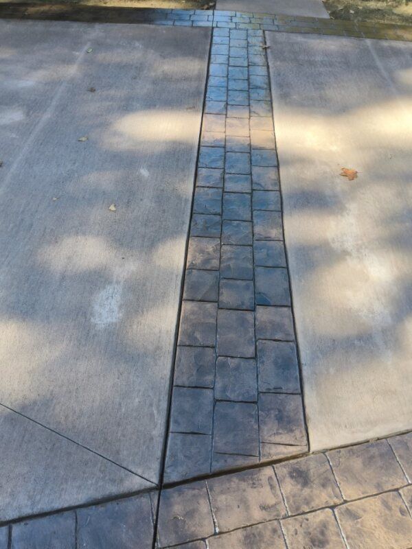Concrete driveway with dark square pavers running down the center and bordering the edges.