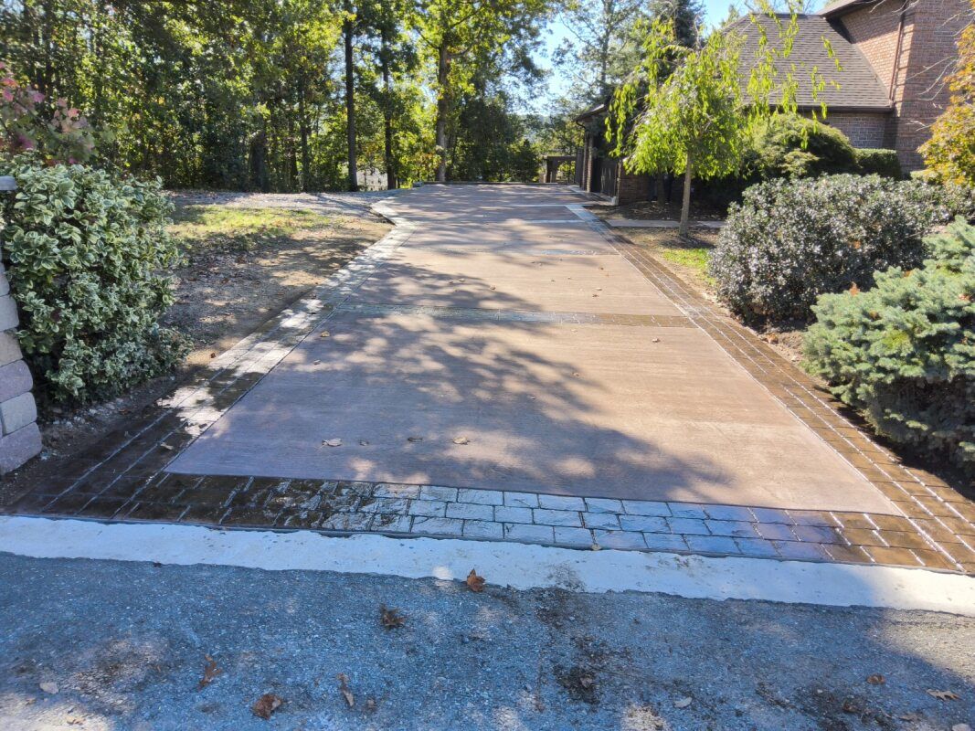Driveway with brick borders and concrete surface leading to a house, surrounded by landscaping.