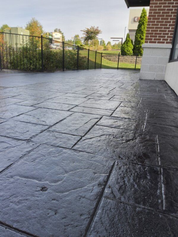 Dark gray stamped concrete patio with stone pattern, brick wall, and black fence.