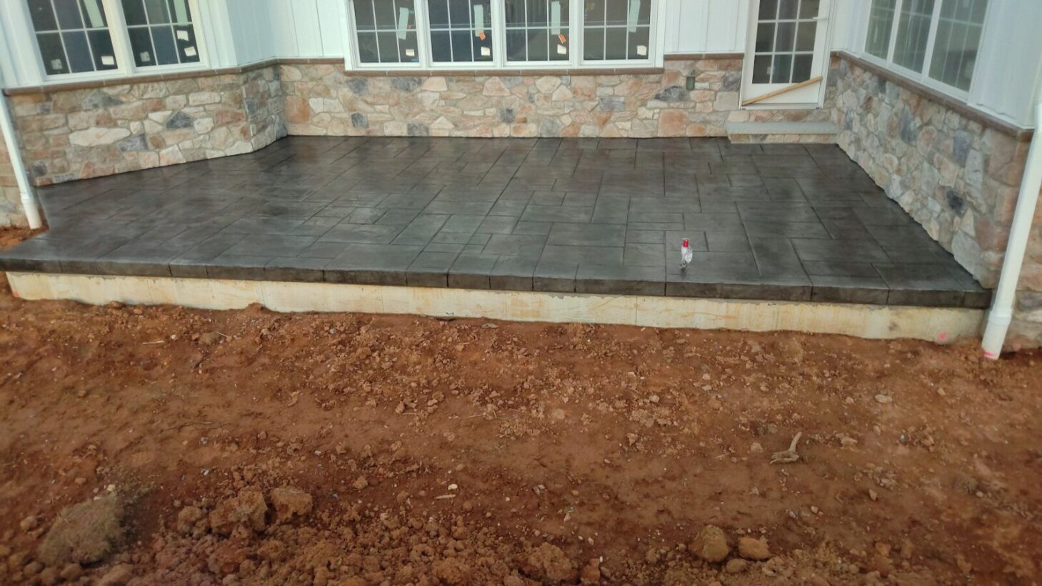 Concrete patio with a wood grain texture, stone walls, and surrounding dirt.