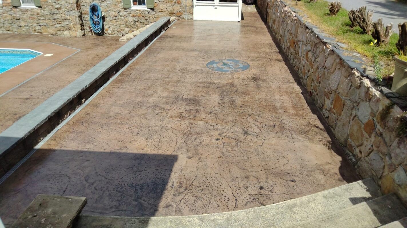 Brown stamped concrete patio with stone walls, near a pool and house.