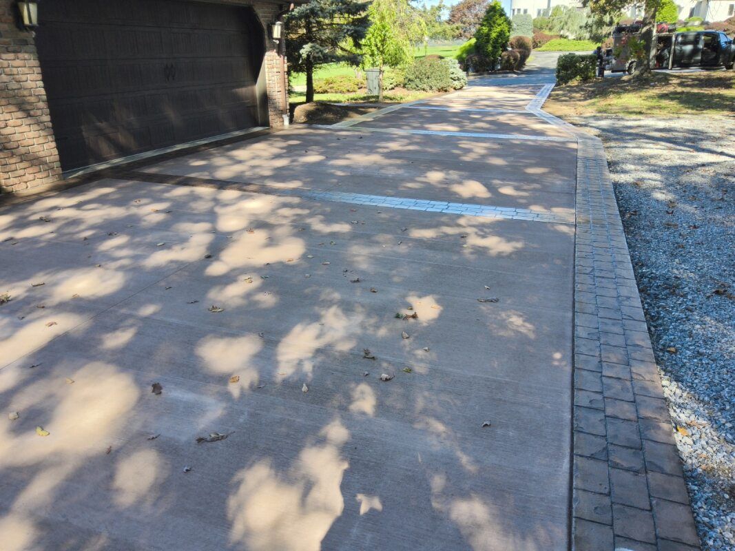 Driveway with shadows from overhead trees, bordered by brick pavers.