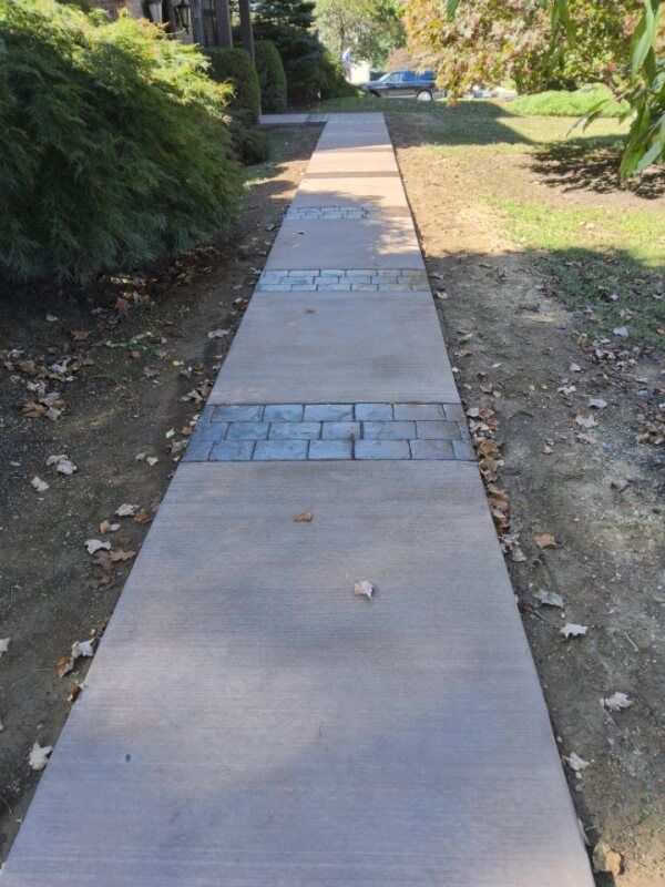 Concrete sidewalk with decorative brick sections, bordered by grass and landscaping.
