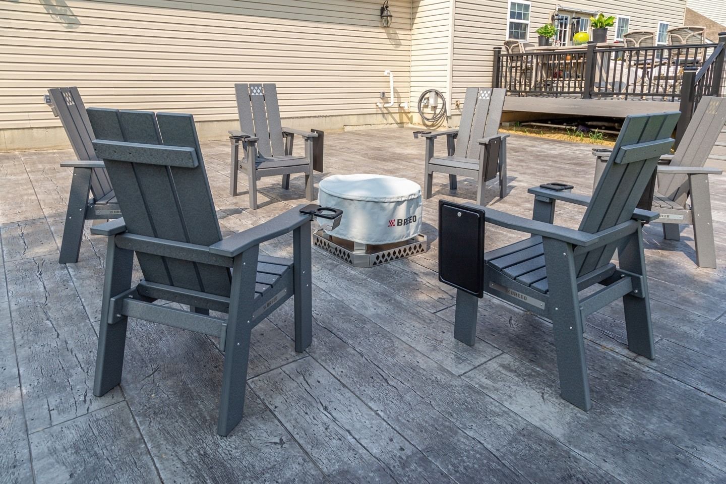 Six gray Adirondack chairs circle a fire pit on a wooden patio.
