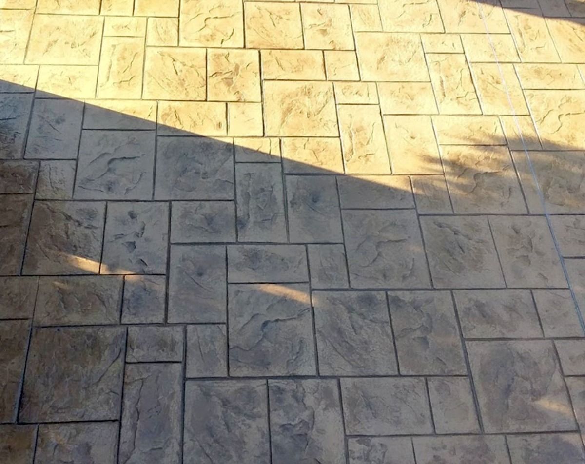 Stamped concrete patio with rectangular stone pattern, shaded by sunlight.