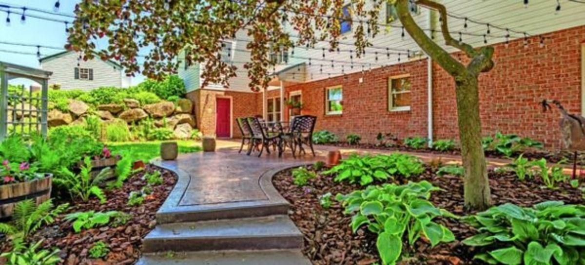 A backyard patio with a dining set, lush plants, and a brick wall.