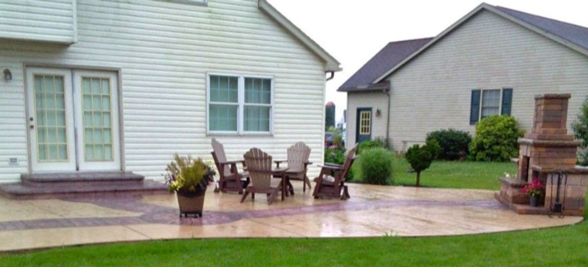 Patio with outdoor furniture, fireplace, and two houses in the background. Green grass.