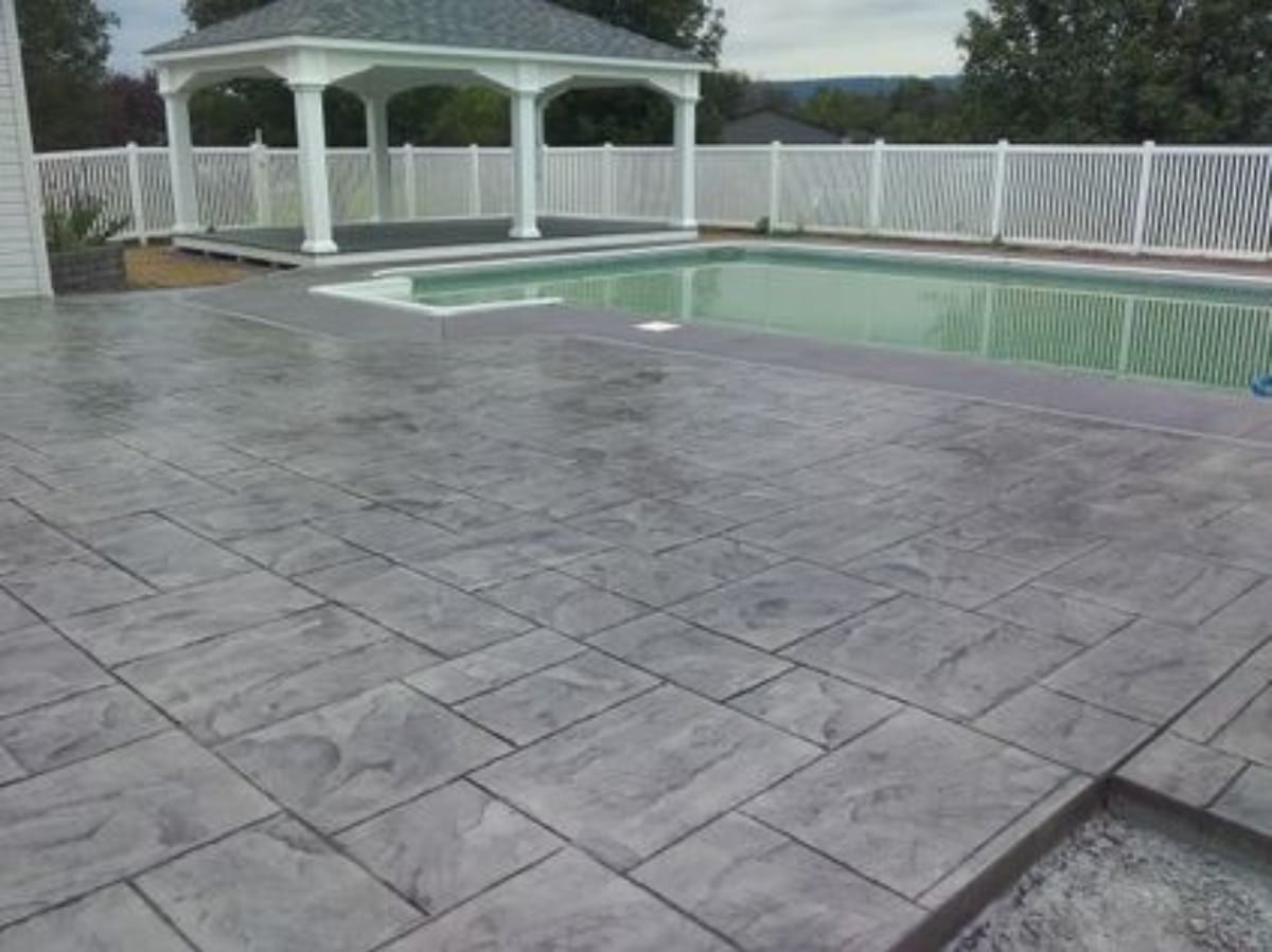 Pool deck with patterned grey concrete, a pool, white gazebo, and fence.