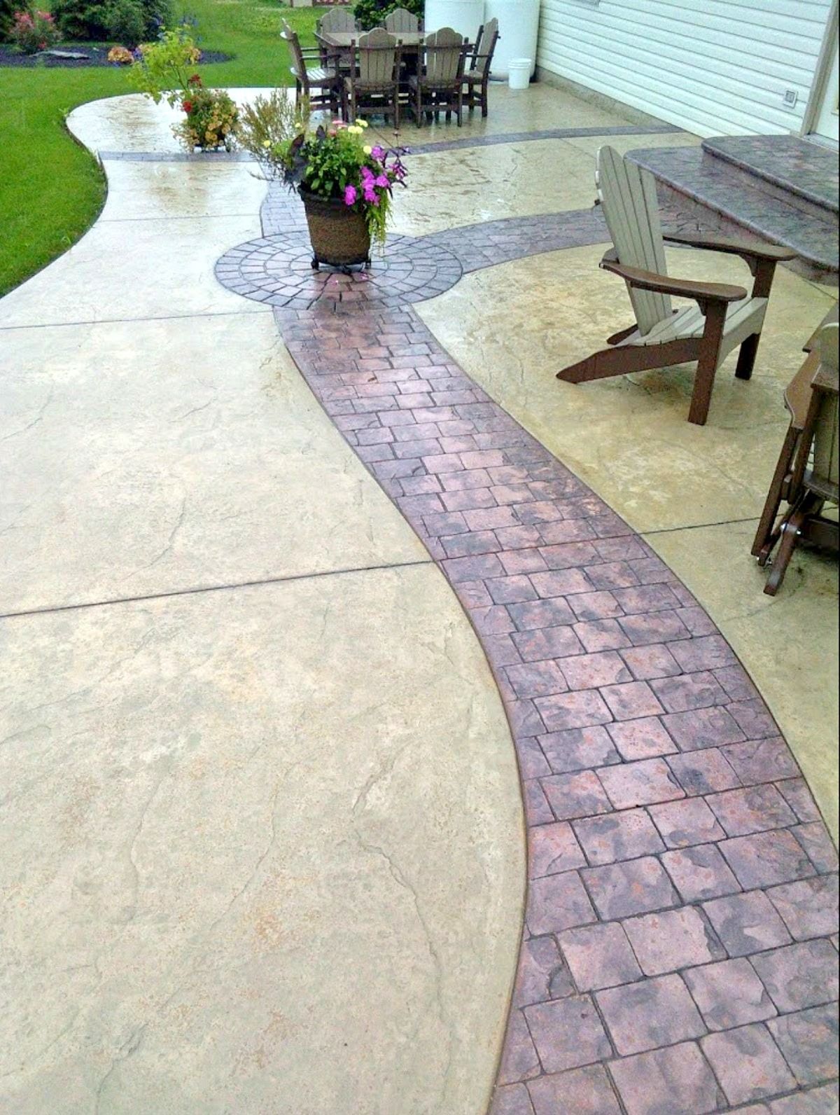 Concrete patio with a brick-like pathway and flower pot, leading to a dining area, sunny outdoor setting.