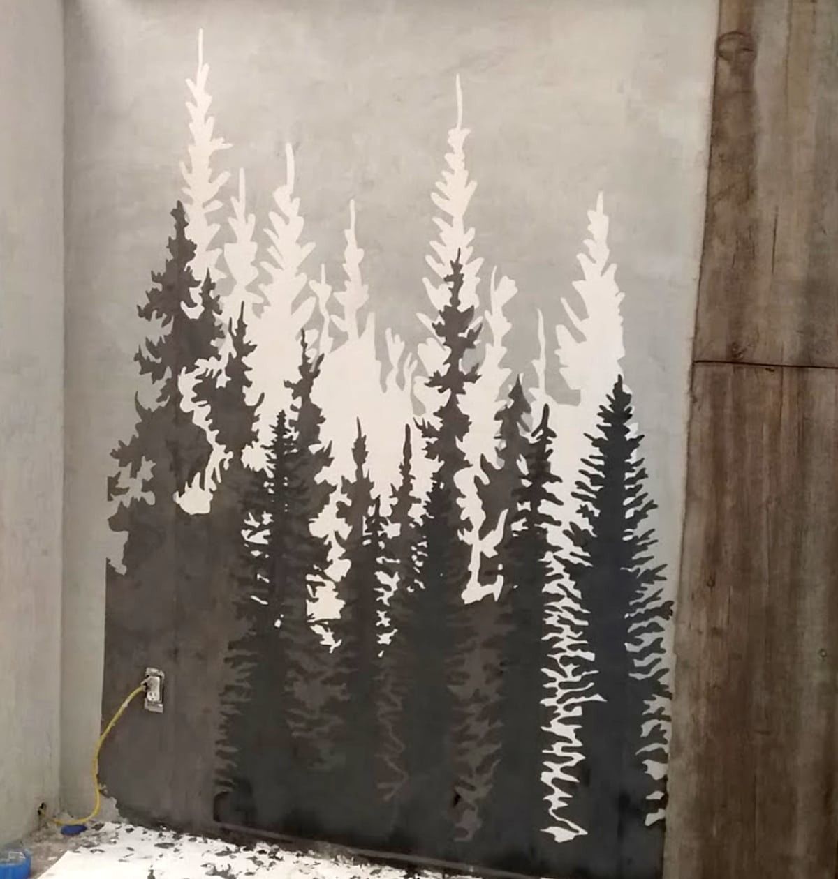 Gray and white forest silhouette painted on a concrete wall, depicting pine trees with varying depths.
