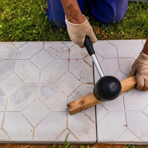 Person using a mallet to align pavers on a grassy surface.