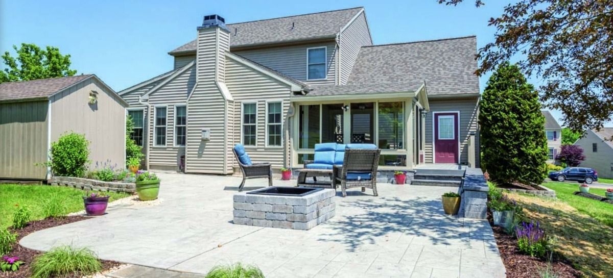 Backyard patio with seating, a fire pit, and a house. Green lawn, blue sky.