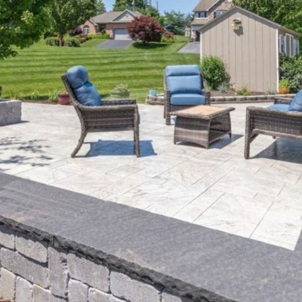 Patio with wicker furniture, stone wall, and manicured lawn.