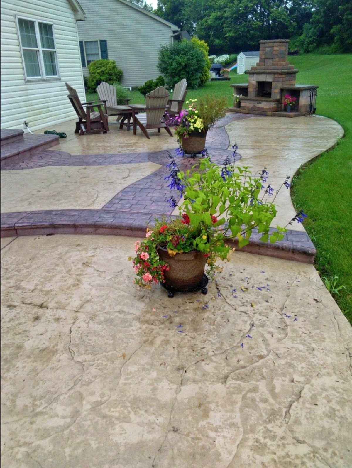 A concrete patio with flower pots, seating area, and outdoor fireplace.