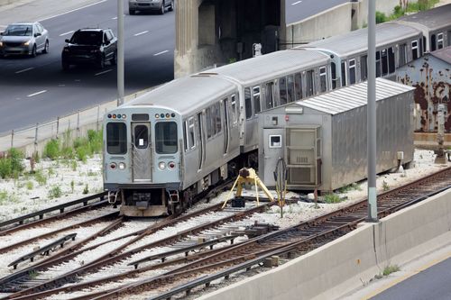 Derailed silver subway train beside tracks near an elevated road and utility shed