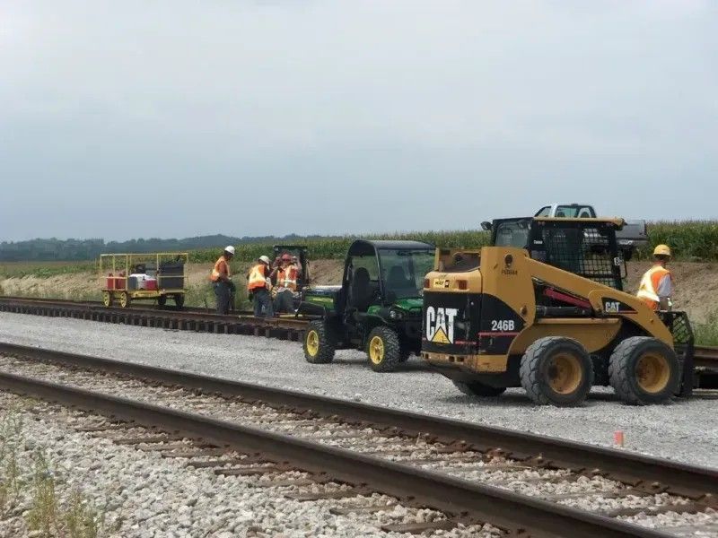 Construction workers and CAT loaders repairing railroad tracks in a rural field