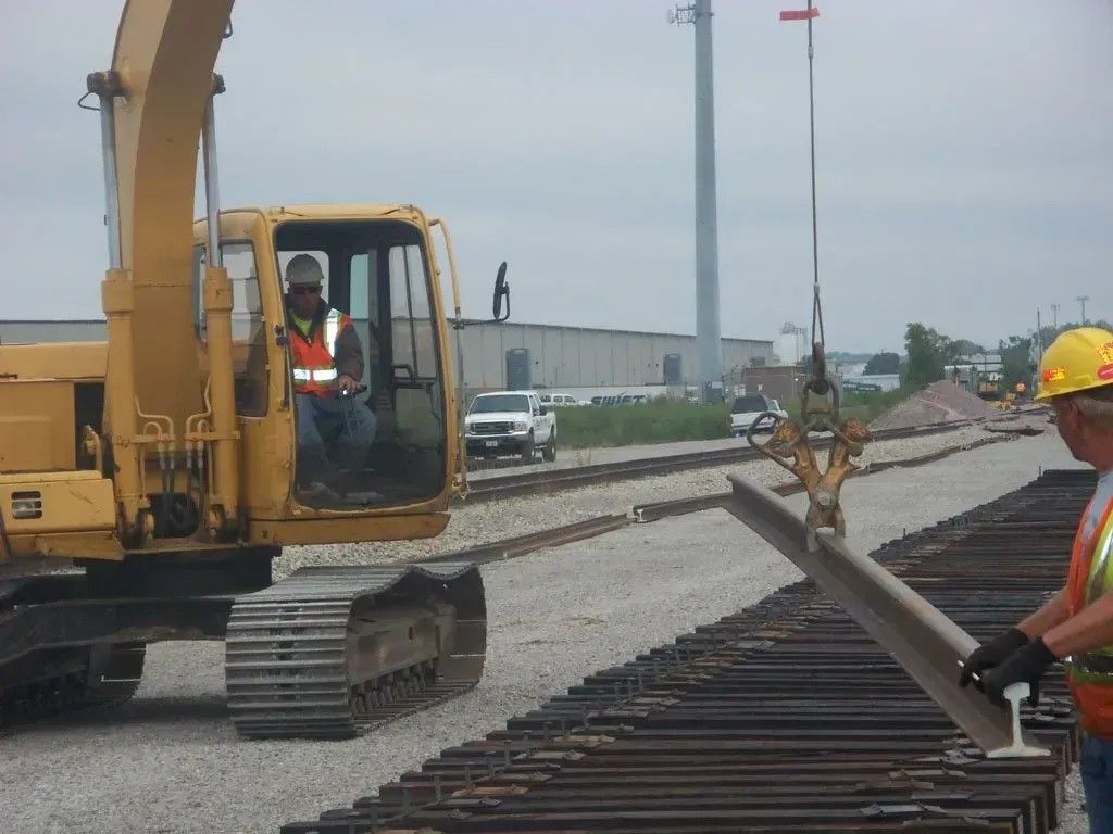 Construction worker operating excavator beside railroad tracks during track maintenance