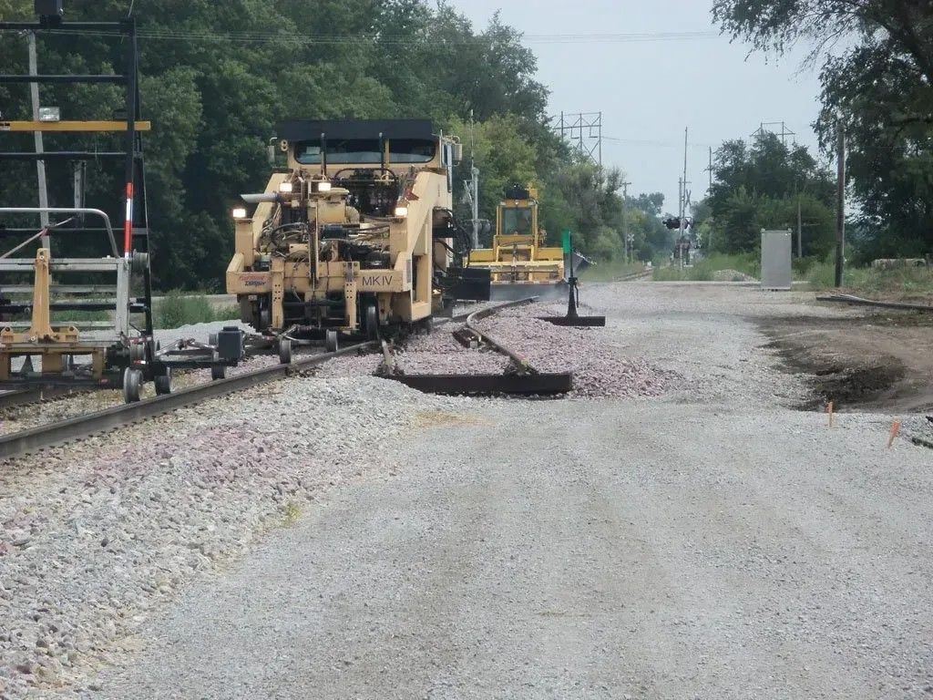 Road construction site with a yellow paving machine spreading gravel on a gravel road