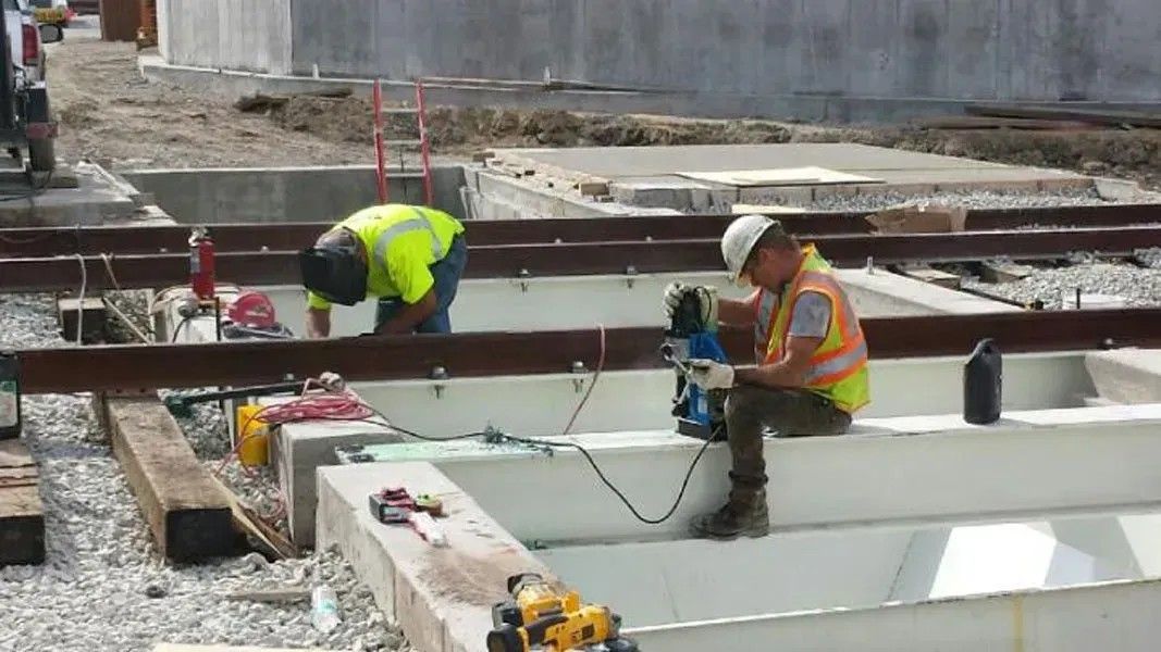 Construction workers in safety vests install concrete beams at an active building site