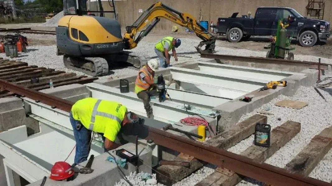 Workers installing white metal beams at a construction site beside excavators and a pickup truck