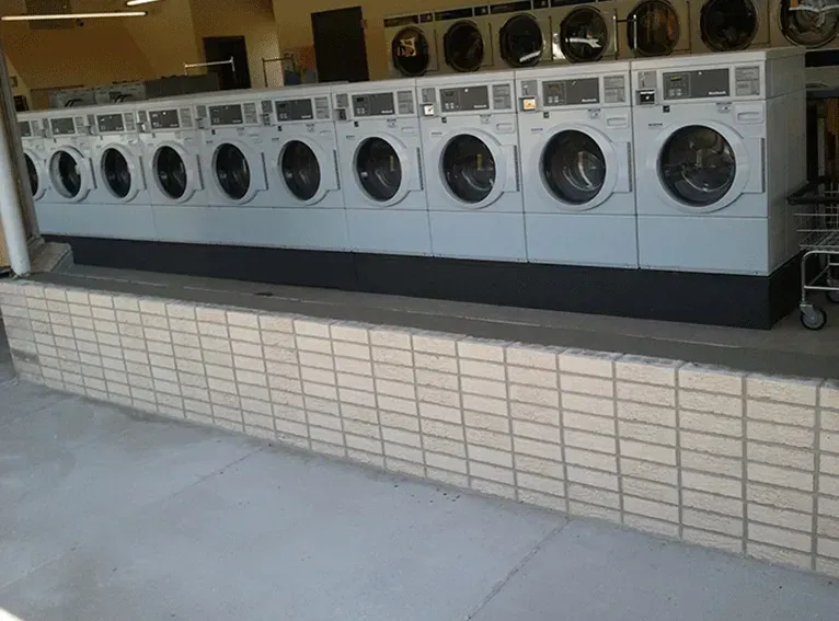 Row of white front-loading washing machines in a laundromat.