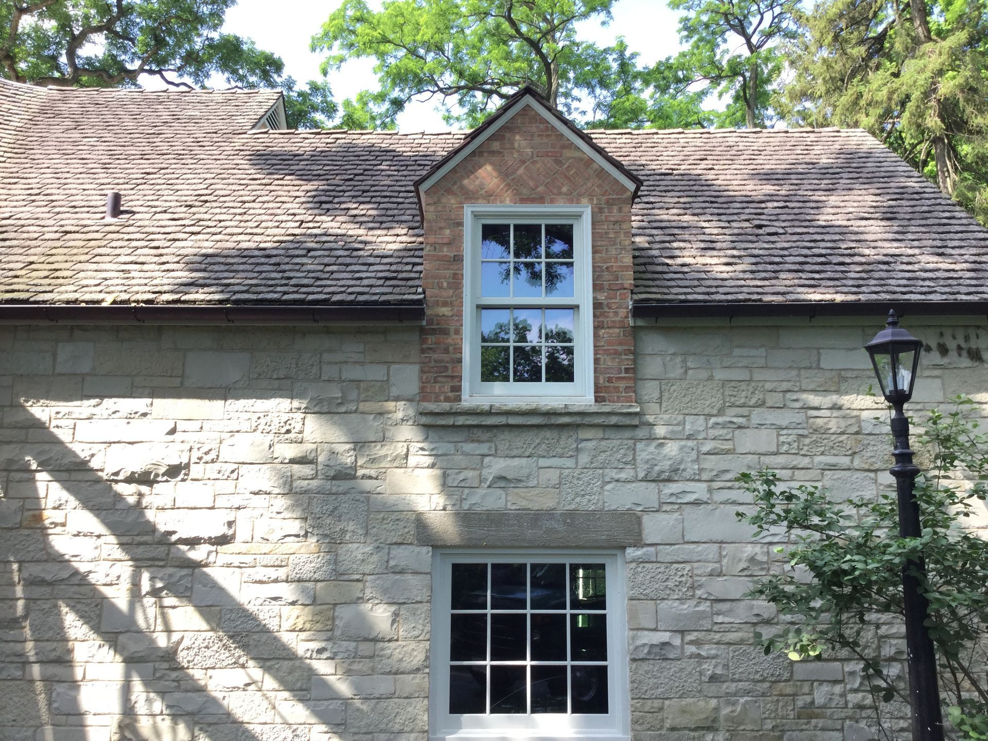 A stone building with a shingled roof, a rectangular ground-floor window, and a gabled dormer with a sash window.