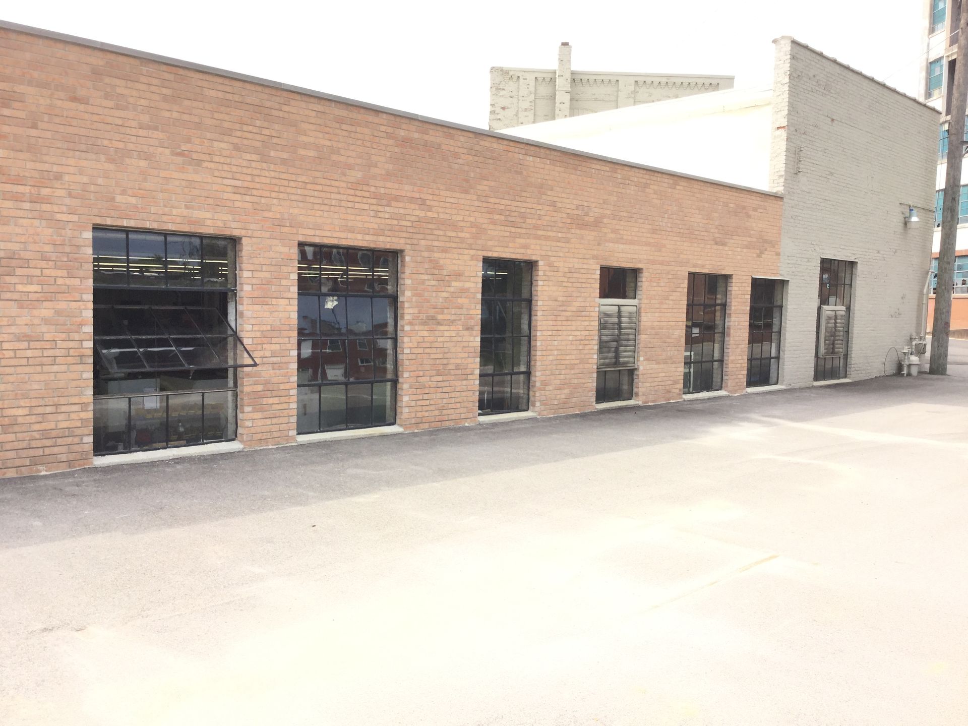 A one-story brick building with six large, dark-framed rectangular windows along a paved area on a bright day.