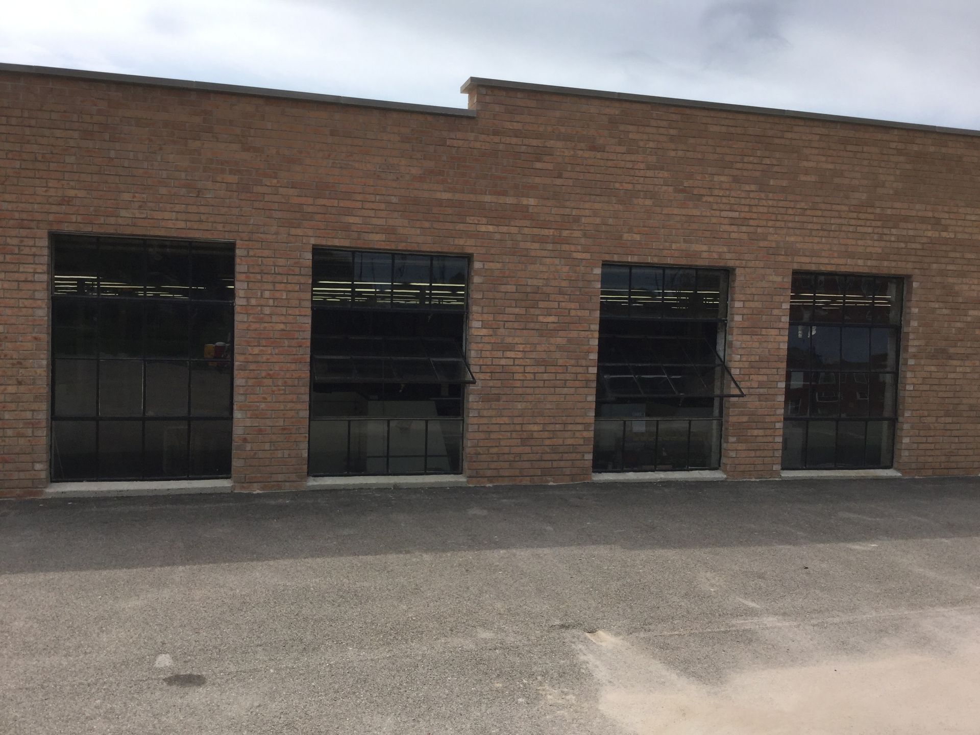 A single-story brick building facade with four large, dark-paned rectangular windows featuring open bottom sections.