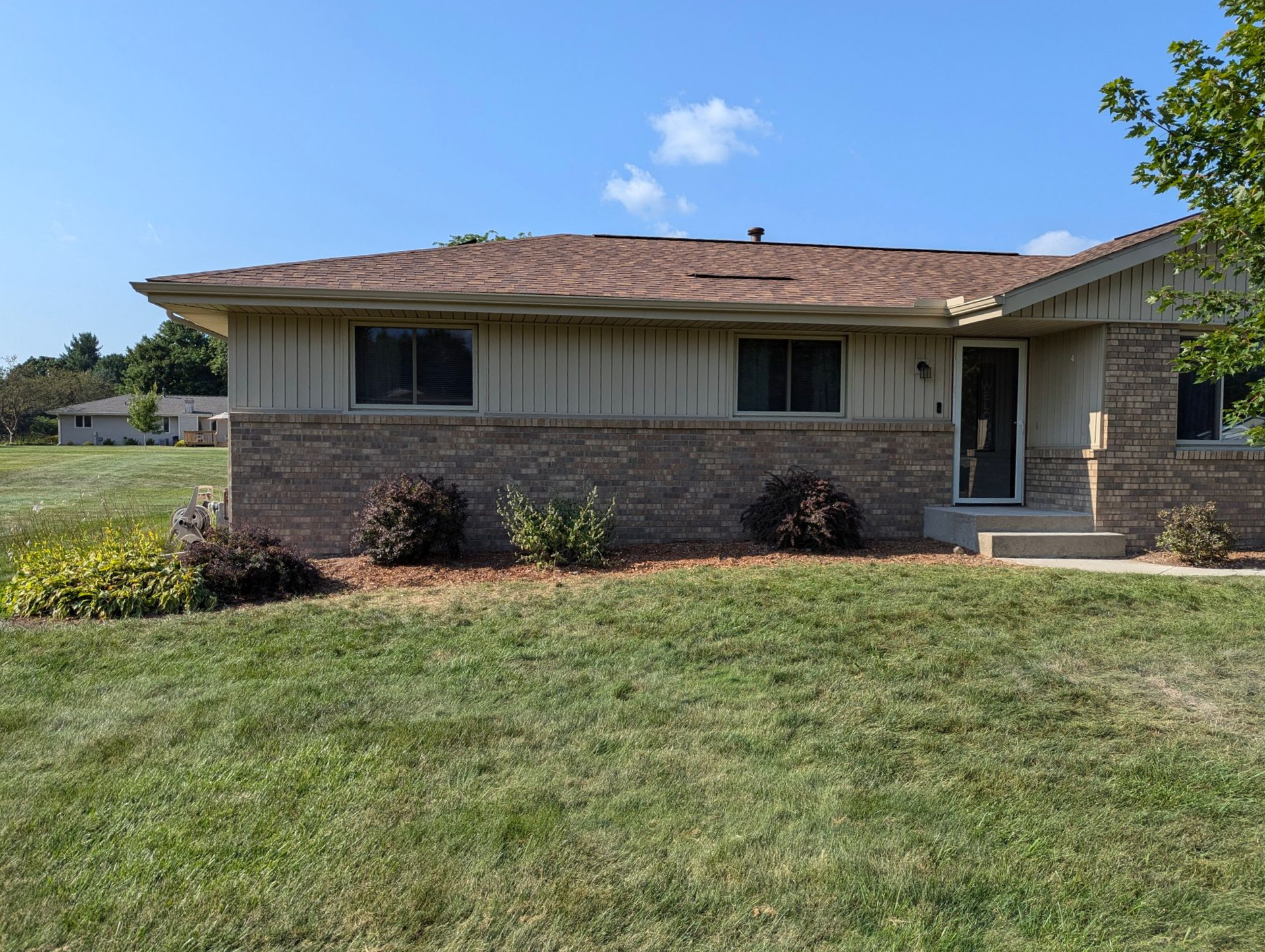 Single-story house with a brick and light-colored siding facade, a brown shingled roof, and a large lawn.