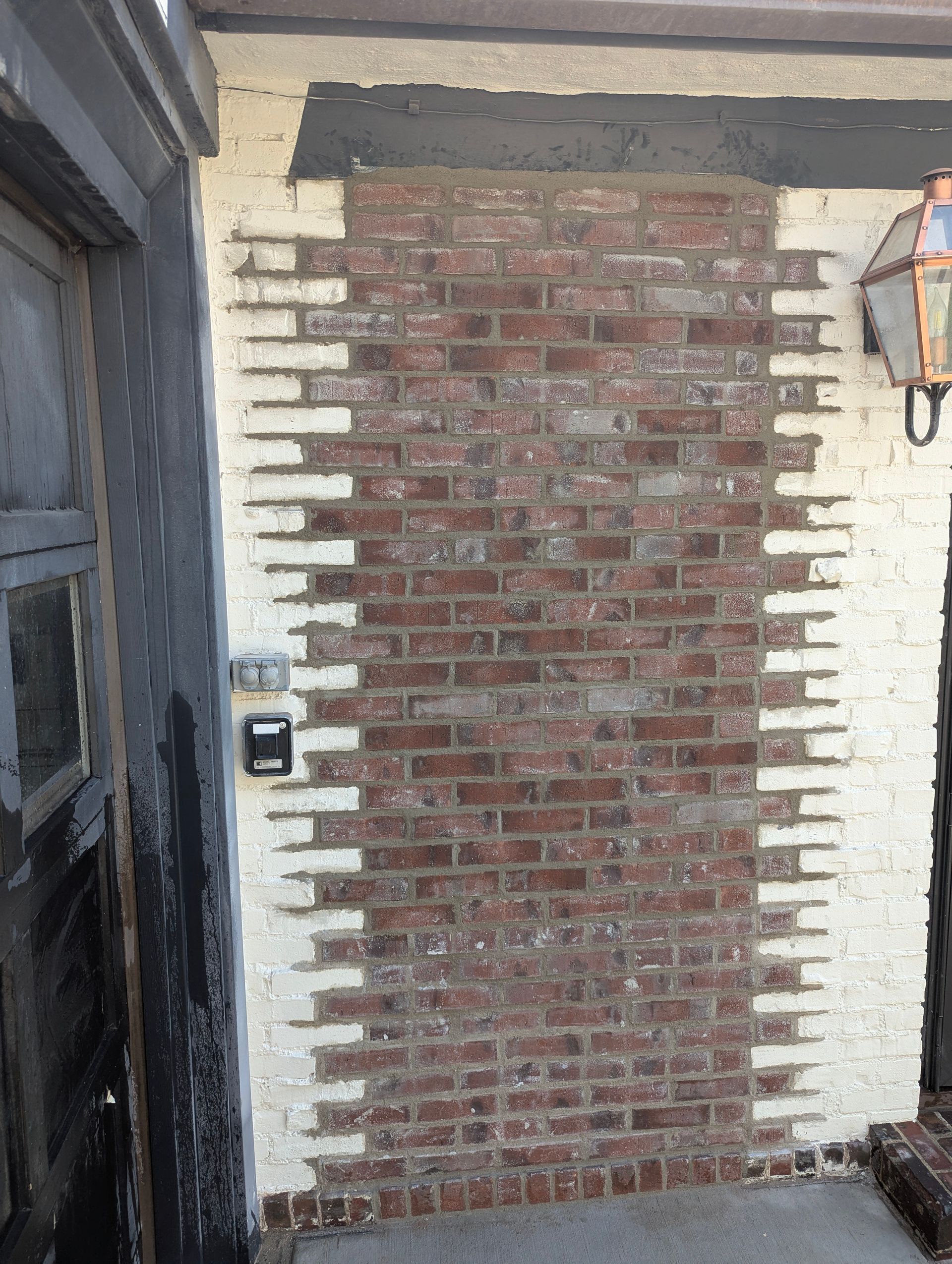 A textured brick wall with a central section of exposed dark red bricks transitioning into white-painted bricks on sides.