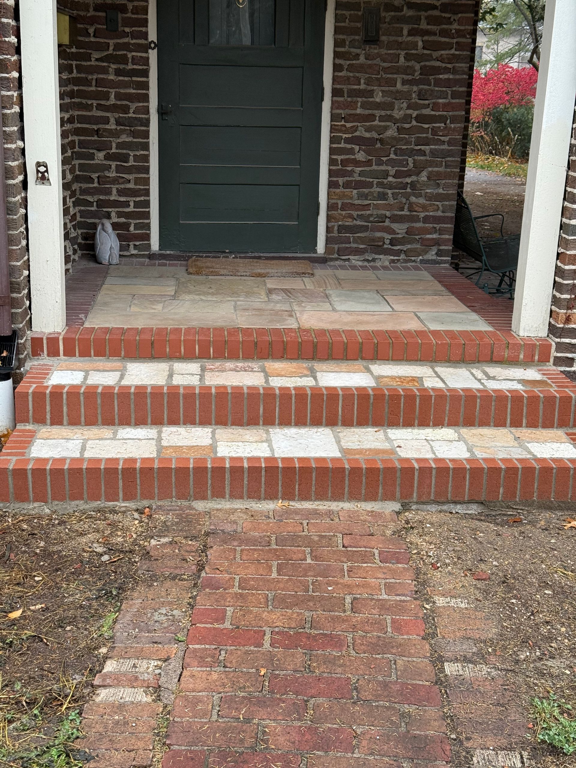A front entrance with three brick-edged stone steps leading up to a dark green door on a brick house.